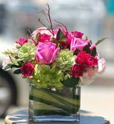 a glass vase filled with pink and green flowers on top of a wooden table next to a car