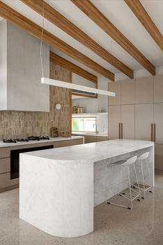 a kitchen with white marble counter tops and wooden beams on the ceiling, along with two bar stools