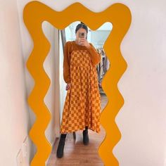 a woman taking a selfie in front of a mirror with an orange and white checkered dress