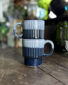 two blue and white coffee cups sitting on top of a wooden table next to each other