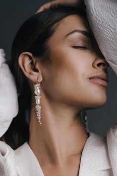 a woman in white sweater holding her head up to her ear and looking off into the distance