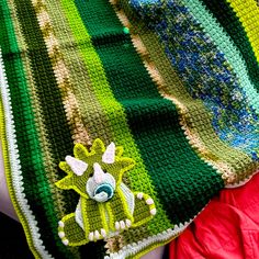 there is a crocheted blanket that has a green and yellow animal on it