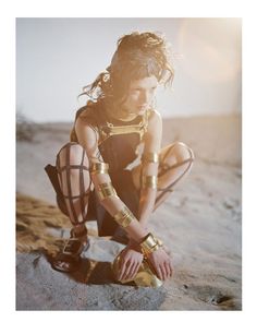 a woman kneeling down in the sand with her hands on her knees and wearing armor