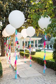 some balloons are hanging from the trees in front of a house with white balls and tassels