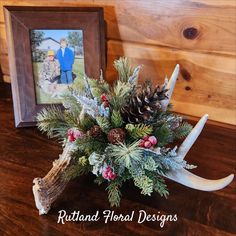 an antler is decorated with pine cones, berries and other greenery next to a framed photograph