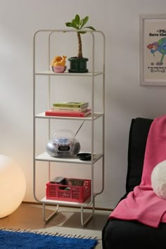 a white shelving unit in a living room next to a blue rug and potted plant