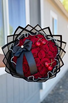 a bouquet of red roses in a black box with a bow on the front and side