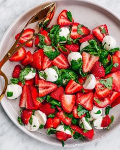 strawberries and mozzarella salad on a white plate with gold utensils