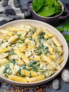 a white bowl filled with pasta and spinach on top of a blue table cloth