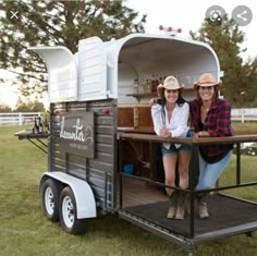 two women are standing in the back of a horse trailer that is parked on grass