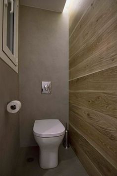 a white toilet sitting inside of a bathroom next to a wooden paneled wall and window