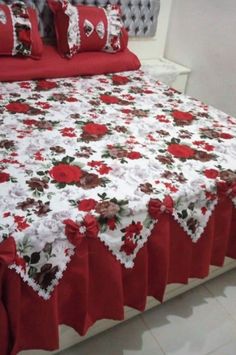 a bed covered in red and white bedspread with flowers on it's edges