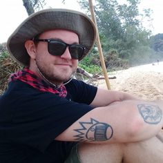 a man wearing sunglasses and a hat sitting on a beach with his arm wrapped around him