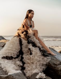 a woman sitting on top of a rock next to the ocean wearing a long dress