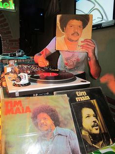 a man holding up a record player in front of some records on a counter top