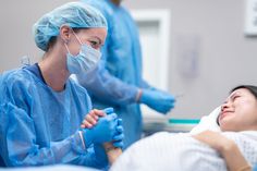 a woman laying in a hospital bed with medical personnel around her and wearing blue gloves