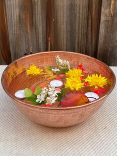 a copper bowl filled with water and flowers on top of a white cloth covered table