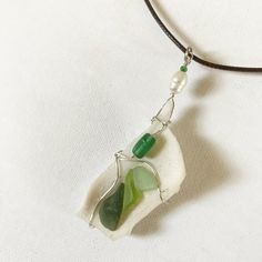 three sea glass pieces are attached to a leather cord on a white surface with a green bead