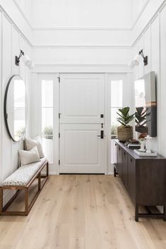 a white hallway with wood floors and a bench in front of the door that leads to another room