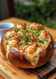 a bread bowl filled with shrimp and cheese on top of a wooden cutting board next to a cup of coffee