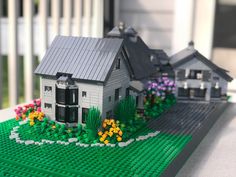 a lego model of a house with flowers in the foreground and two houses on the other side