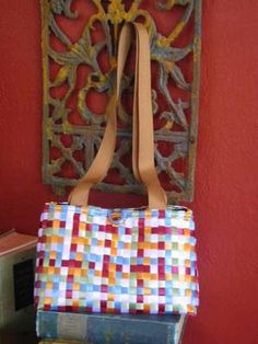 a multicolored tote bag sitting on top of a stack of books in front of a red wall