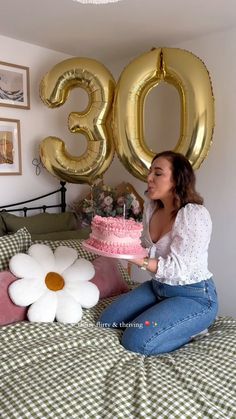 a woman sitting on a bed with a cake and balloons in the shape of 50