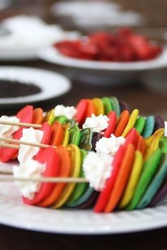 colorful food on skewers sitting on top of a white plate with other plates in the background