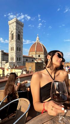 a woman sitting at an outdoor table with a glass of wine