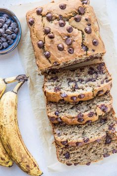 sliced banana bread with chocolate chips on top next to a bowl of blueberries and two bananas