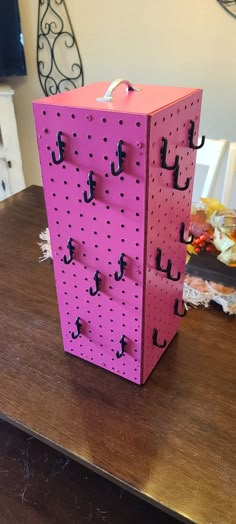 a pink pegboard with hooks on it sitting on top of a wooden table next to a vase