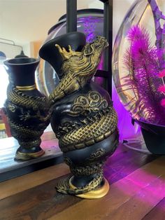 two vases sitting on top of a wooden table next to purple flowers and plants