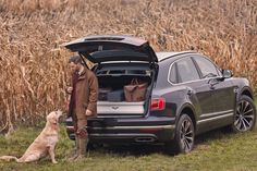 a man standing next to a car with its trunk open and a dog looking at it