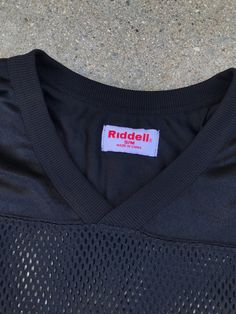 "Rock this amazing vintage black mesh jersey with a bold black leather pencil skirt. 100% Polyester Features modern aesthetic Brand: Riddell Estimate Size: M/L Listed Size: S/M Length: 24\" Bust: 46\" Waist: 46\"" 90s Style Black Tops For Fall, Black Mesh Top For Fall, Black Stretch 90s Style Tops, 90s Style Black Stretch Tops, 90s Style Stretch Black T-shirt, Sporty Black Jersey With Graphic Print, Black Stretch 90s Style T-shirt, Sporty Black Top With Mesh Sleeves, Black Sporty Top With Mesh Sleeves