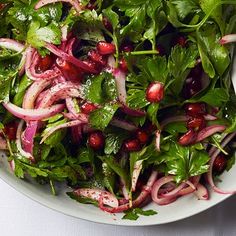 a white bowl filled with green salad and red onions next to a spoon on a table