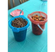 two plastic cups filled with cereal and pretzels on a tablecloth covered table