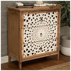 a wooden cabinet with carvings on the front and side drawers, along with a potted plant next to it