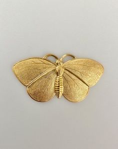 a gold colored butterfly brooch sitting on top of a white surface with no background