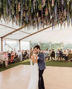 a bride and groom share their first dance under the tented ceiling with flowers hanging from it