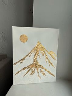 a white canvas with gold foil on top of it and a mountain in the background