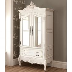 an ornate white armoire with mirrored doors and drawers in a room that has wood flooring