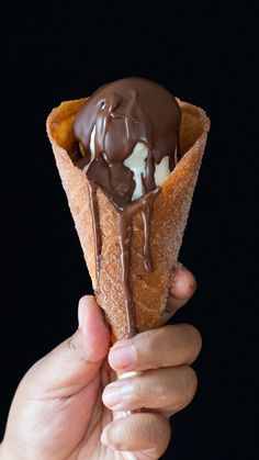 a hand holding an ice cream cone with chocolate on top and drizzled in the middle