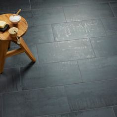 a small wooden table sitting on top of a gray tile floor next to a chair