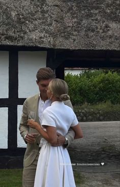 a man and woman standing next to each other in front of a thatched building