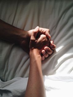 two people holding hands on top of a bed