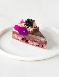 a piece of cake on a white plate with purple flowers and blackberries in the middle