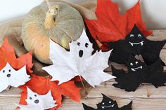 some leaves and pumpkins are sitting on a wooden surface with faces painted on them