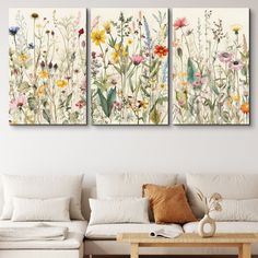 two floral paintings hanging on the wall in a living room with white furniture and pillows