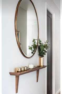 a mirror hanging on the wall above a shelf with candles and a potted plant