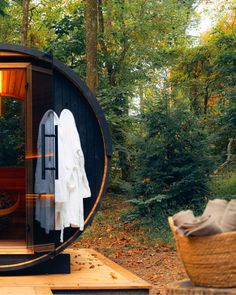 an outdoor sauna in the woods with towels hanging on it's side and a basket next to it